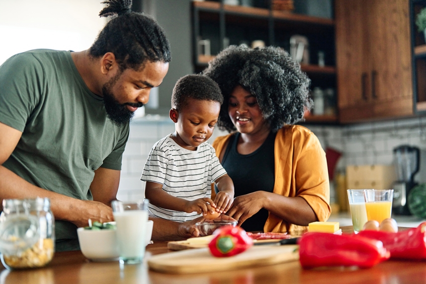A man and woman are cooking with a young child 